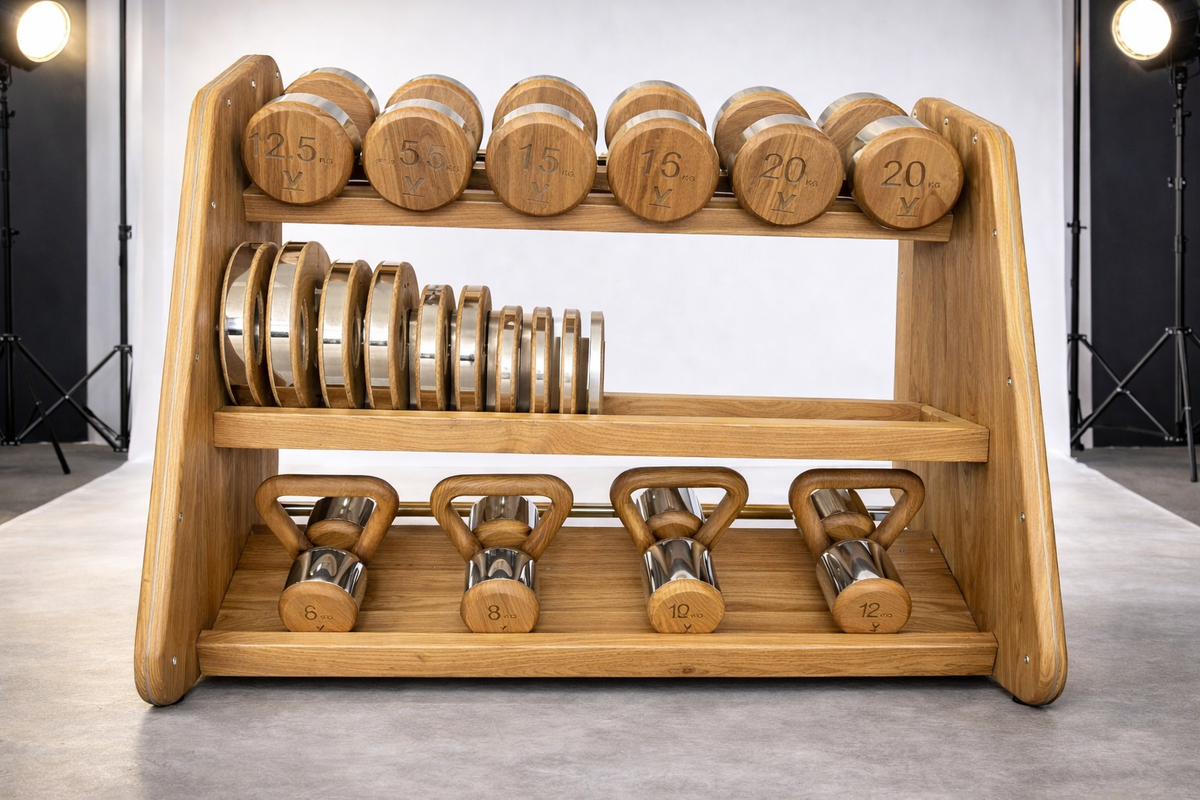 A wooden multi-functional dumbbell rack holding wooden dumbbells, weight plates, and kettlebells, set against a studio backdrop with visible studio lights in the background.